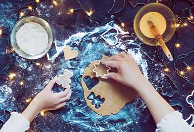 Dos personas cortando en figuras una masa para galletas. 