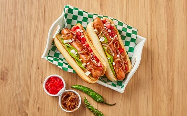 Plato con hot dogs, cebollas caramelizadas, tomates y ajíes