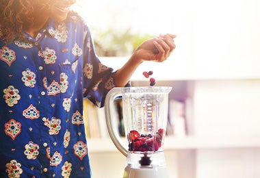 Mujer preparando acaí bowl añadiendo frutas en licuadora