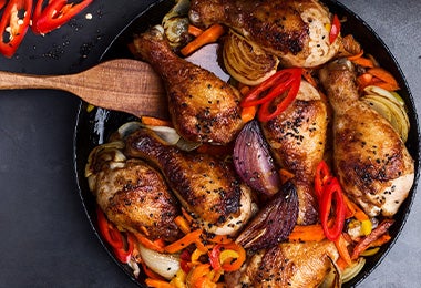 Sartén de hierro con muslos de pollo y verduras.