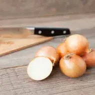 Tabla de corte y cuchillo con cebollas enteras y en mitades  